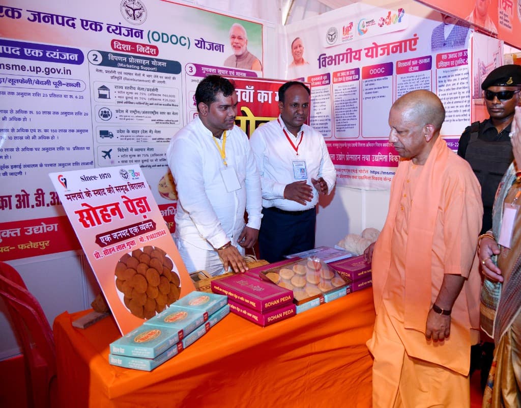 Uttar Pradesh Chief Minister Yogi Adityanath beside the Sohan Peda counter, with boxes of peda and a Since 1970 stall board. Two other men stand at the counter.